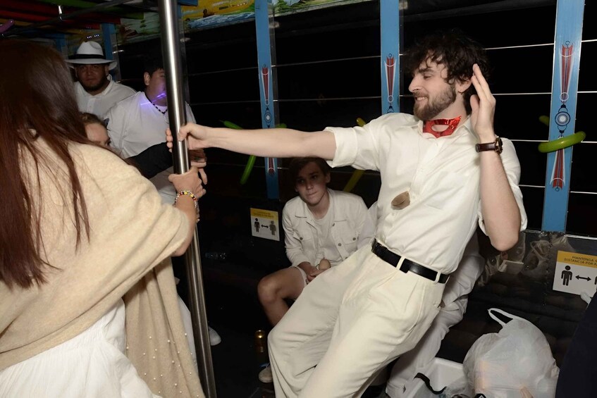 A person in a white shirt and red tie holding onto a pole, with another person in white attire seated nearby. 2