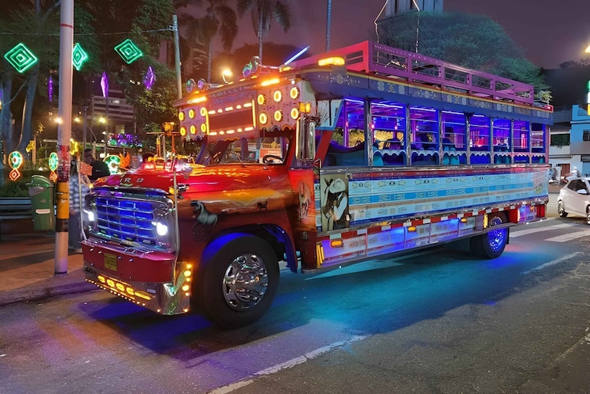 A brightly lit, colorful truck with decorative lights and patterns, parked on a street at night. 1