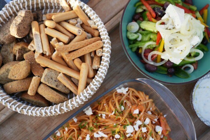 A wooden table with bowls of food, including a salad with cucumbers, red peppers, and white cheese, and a bowl of breadsticks. 5