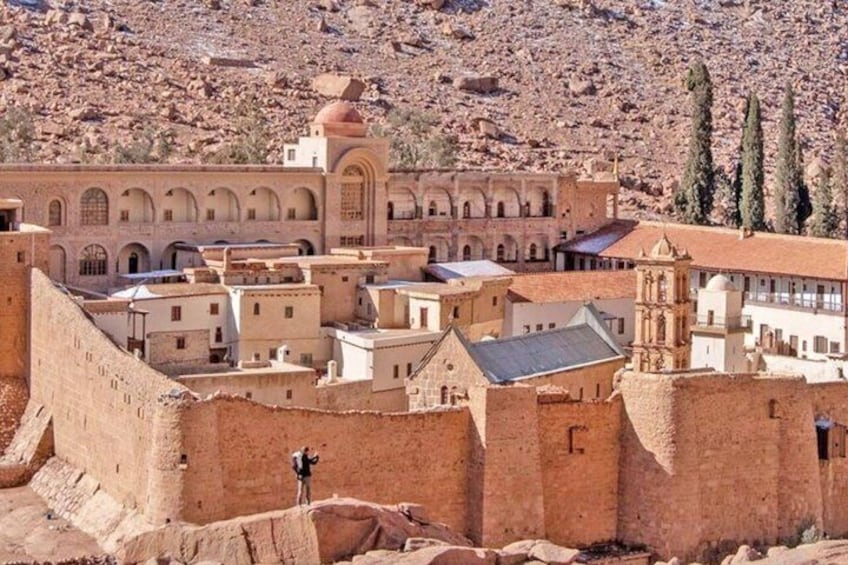 A historic walled city with traditional architecture, including a prominent mosque with a dome and minarets, set against a rugged mountainous backdrop. 1