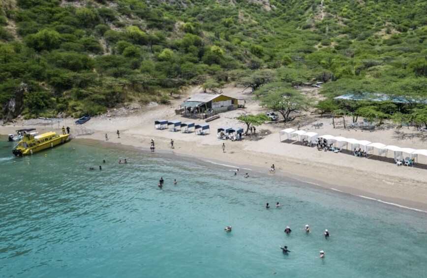 A beach with people swimming and a yellow boat docked near the shore. 2