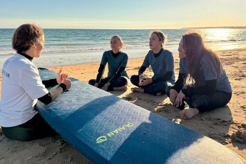 Four people sitting on a blue surfboard on a beach with the ocean in the background. 5