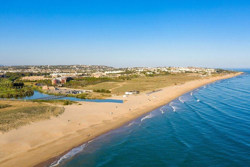 A coastal landscape with a sandy beach, a calm sea, and a distant town. 4