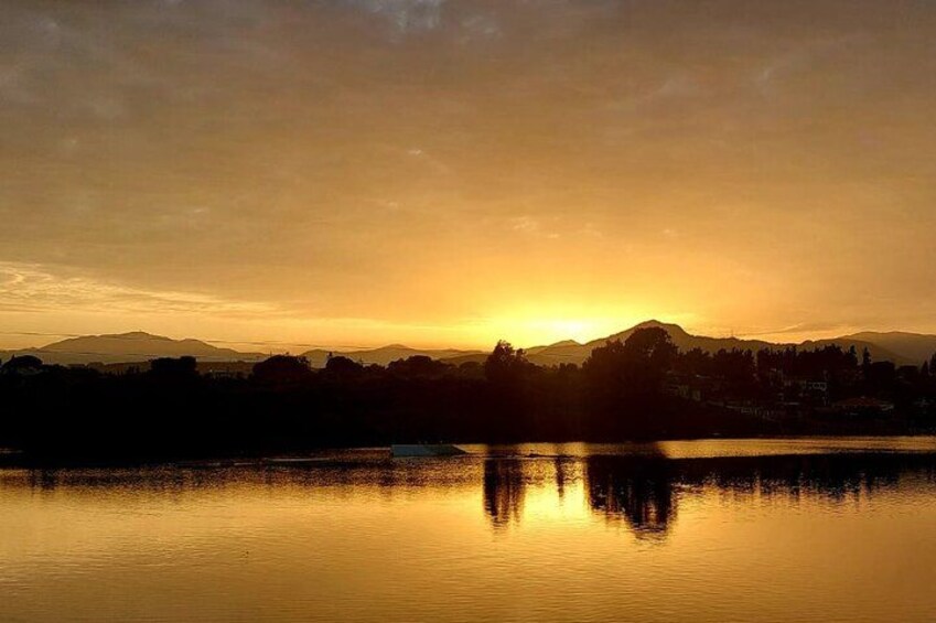 A sunset over a calm lake with silhouettes of buildings and mountains in the background. 2