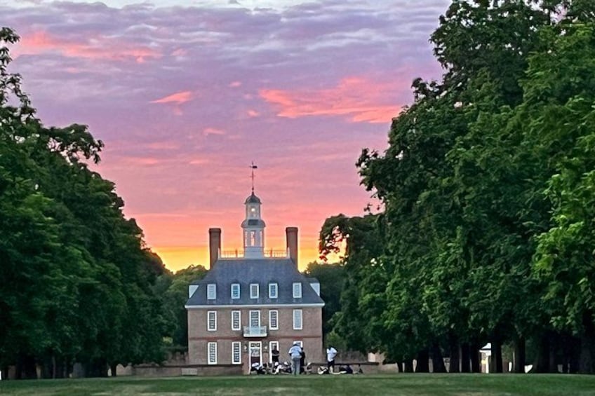 A historic building with a clock tower, surrounded by lush green trees and a sunset sky. 4