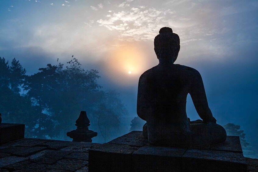 A seated stone statue in a misty landscape with a sun in the background. 1