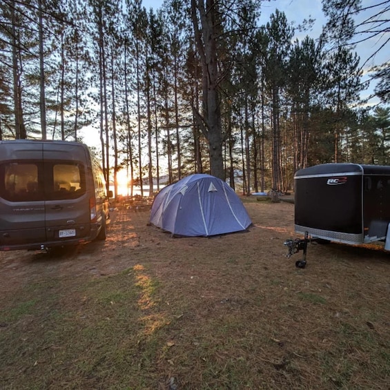 A camping scene with a tent, a van, and a trailer in a forest. 2