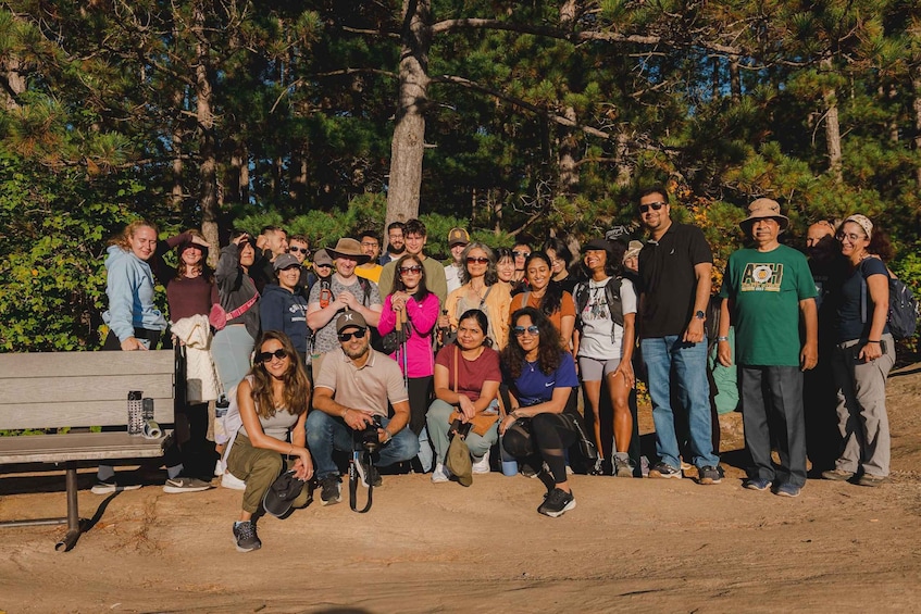 A group of people posing outdoors with trees and a bench in the background. 1