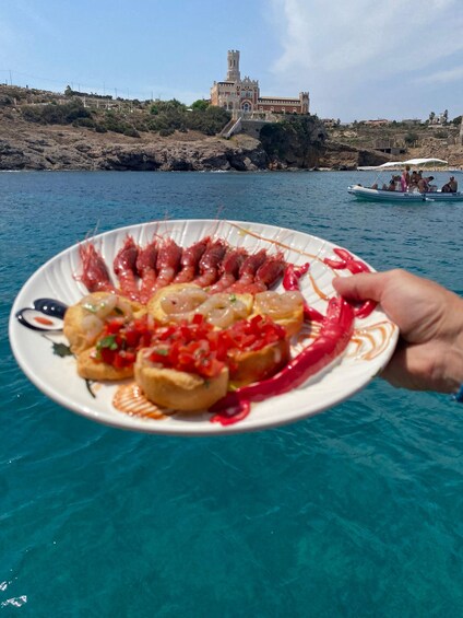 A plate of food with shrimp and bread, held in front of a body of water with a castle in the background. 5