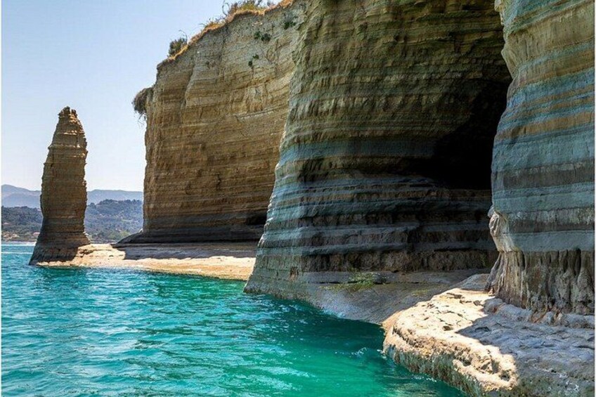 A coastal landscape with layered rock formations and a clear blue sea. 2