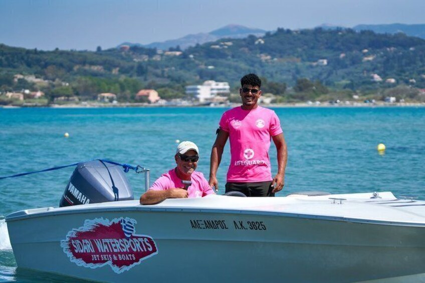 Two people on a boat with a logo for 'Sail Watersports' and a mountainous landscape in the background. 2