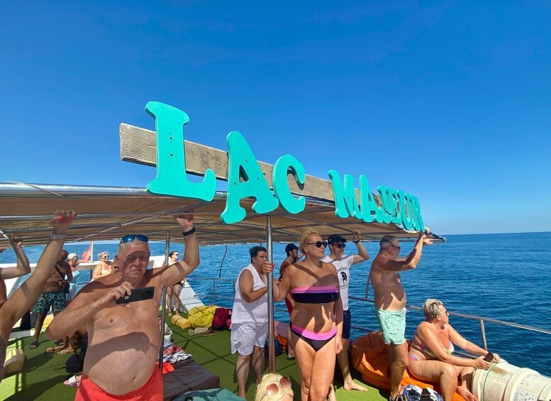 A group of people on a boat with a sign reading 'LAC MAURER' in the background. 5