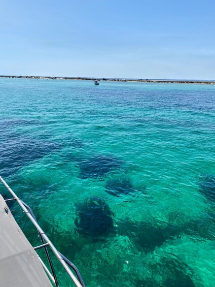 A boat on clear turquoise water with a rocky seabed and a distant shoreline. 4
