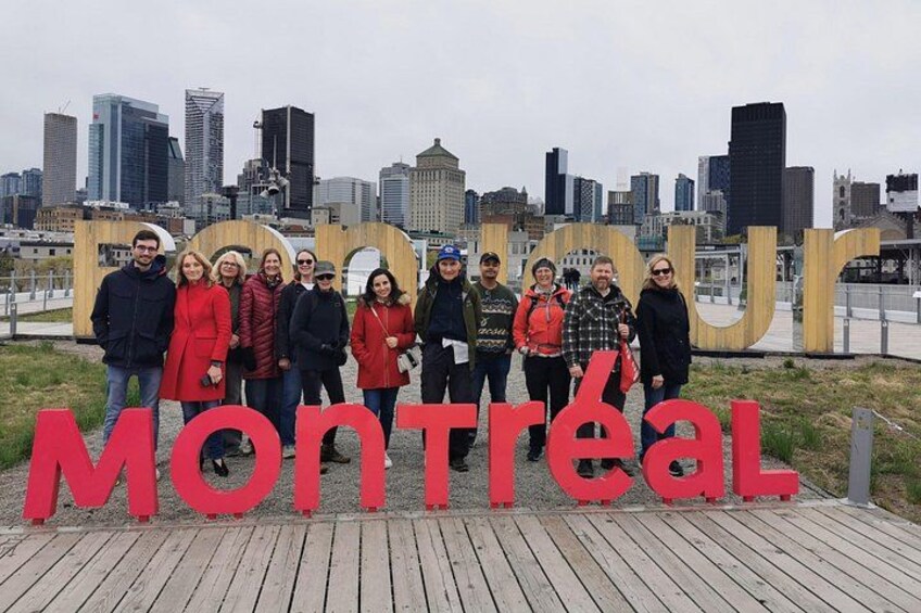A group of people standing in front of a large sign with the word 'Montreal' and the city skyline in the background. 1
