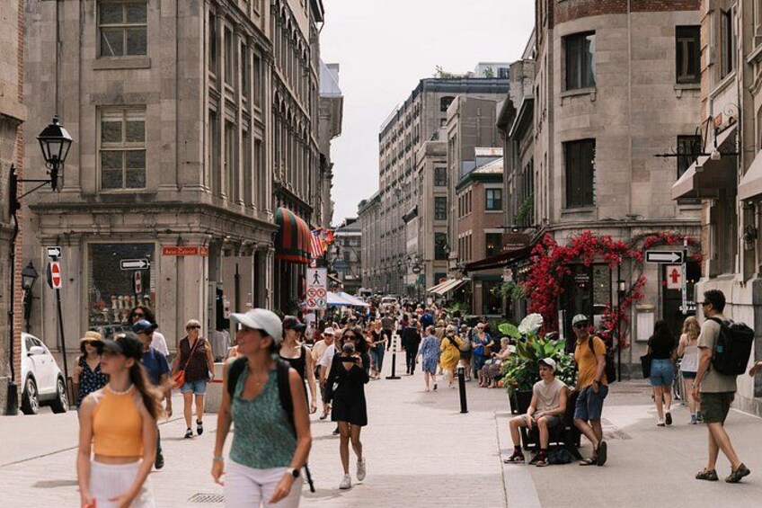 A busy urban street with pedestrians, buildings, and outdoor seating areas. 2