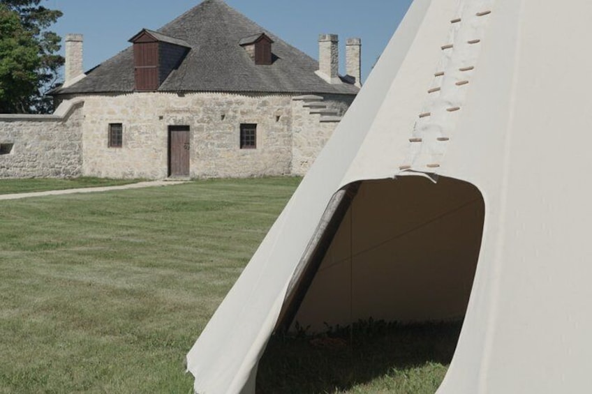 A stone building with a pitched roof and chimneys, a grassy field, and a white tent with a visible entrance. 1