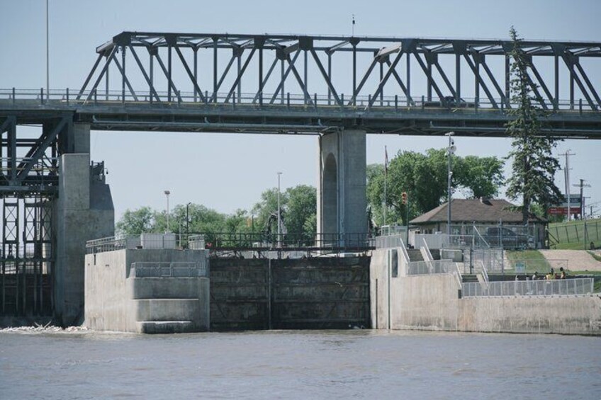 A steel bridge over a river with concrete structures and a building in the background. 5