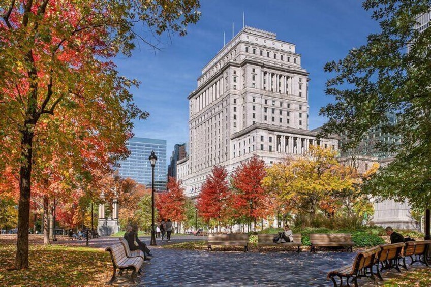 A park with autumn foliage, benches, and a large building in the background. 2