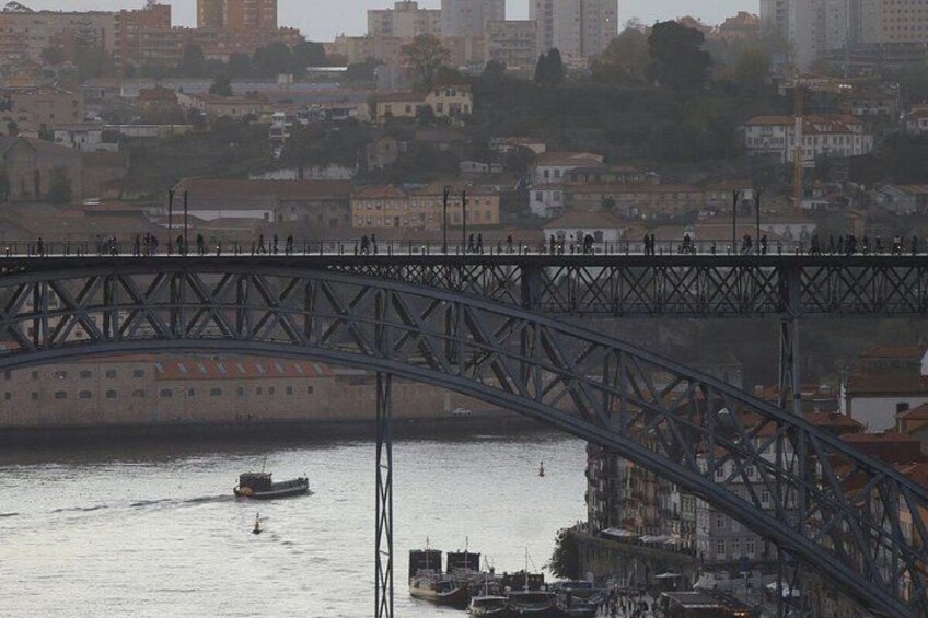 A steel bridge over a river with boats, buildings, and a cityscape in the background. 2