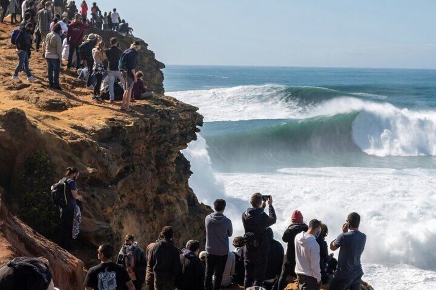 A cliff with people observing waves crashing below. 4