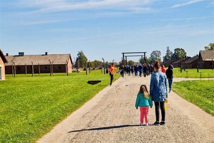 A historical site with a dirt path, brick buildings, and a group of people walking. 2