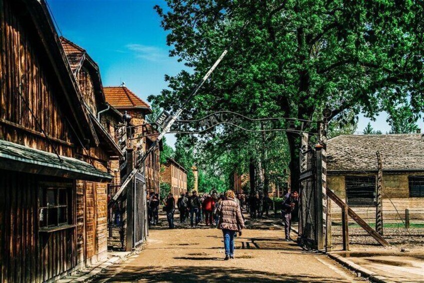 A wooden street lined with buildings, a person walking, and a crowd in the distance. 3