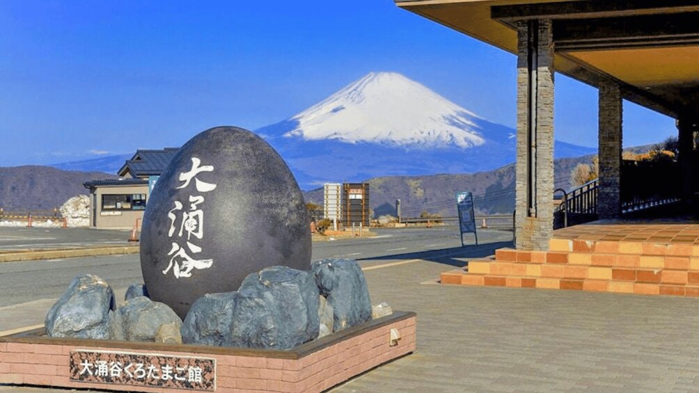A large stone with Japanese characters, a stone wall, a building, and a snow-capped mountain in the background. 3