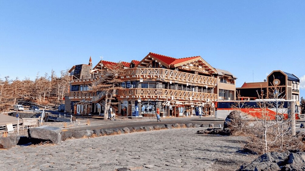 A multi-story wooden building with a red roof, situated in a rocky area with sparse vegetation. 5