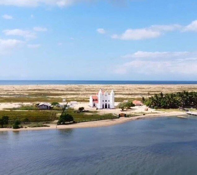 A coastal church with a white facade and red roof, surrounded by a sandy beach and palm trees. 3
