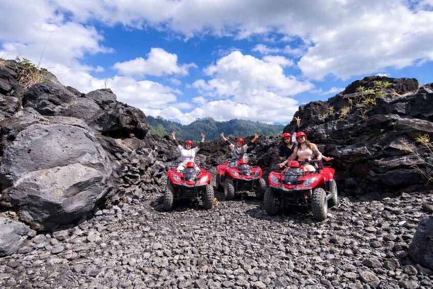 Four people on red ATVs on a rocky terrain with mountains in the background. 2