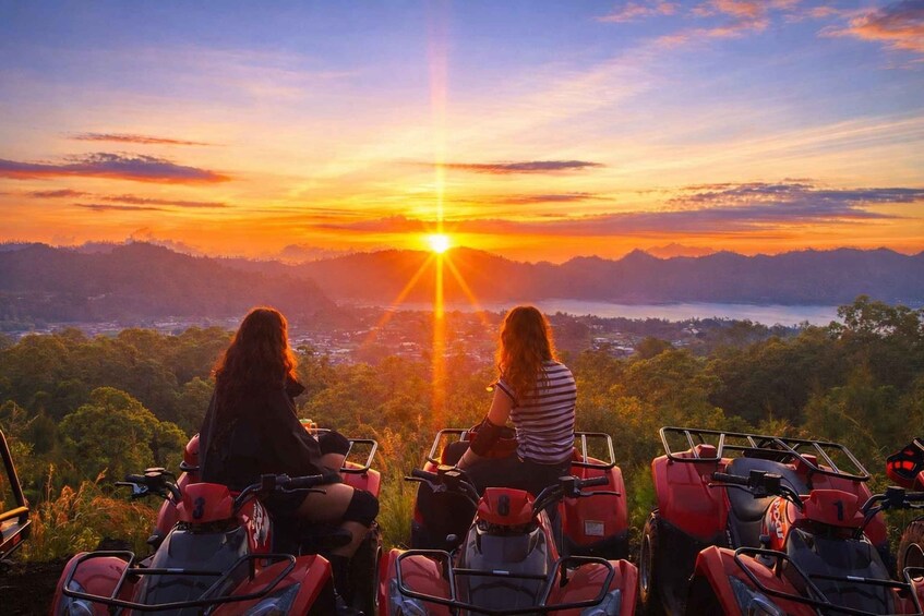 Two people on ATVs overlooking a sunset with a mountainous landscape. 5