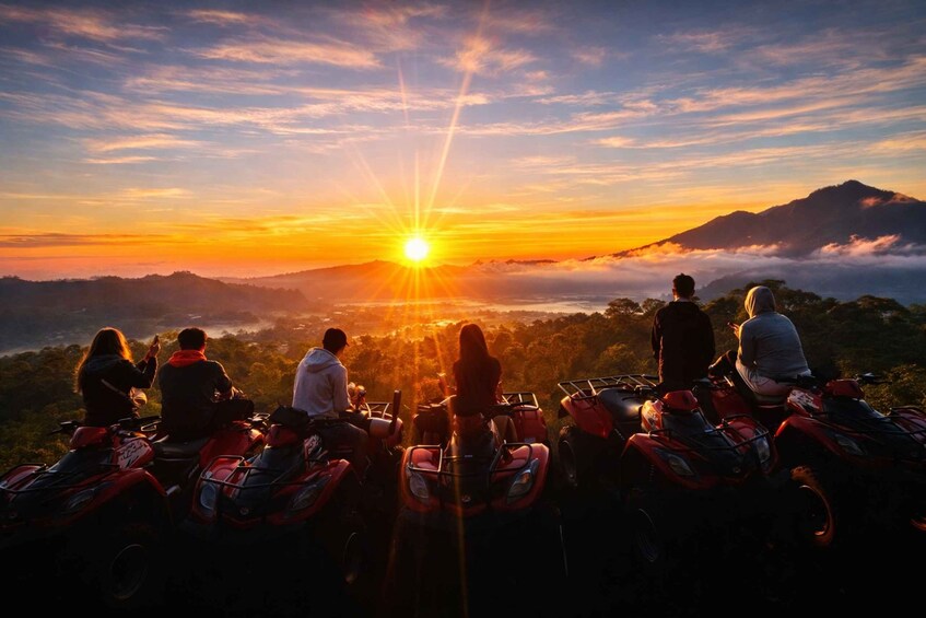 A sunset over a mountainous landscape with people on ATVs. 3