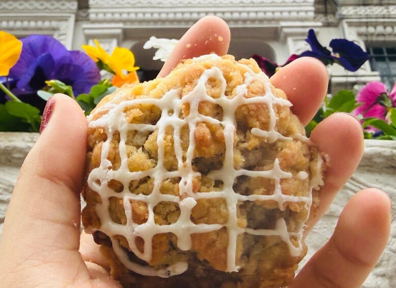 A hand holding a baked good with a grid pattern and white icing, with flowers in the background. 5