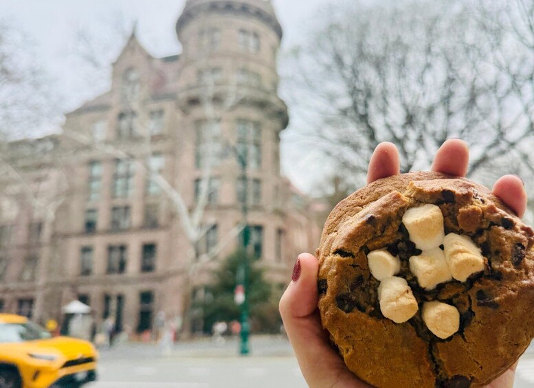 A hand holding a cookie with marshmallows, with a historic building in the background. 2