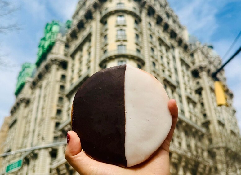 A hand holding a half chocolate and half vanilla ice cream cone in front of a historic building. 1
