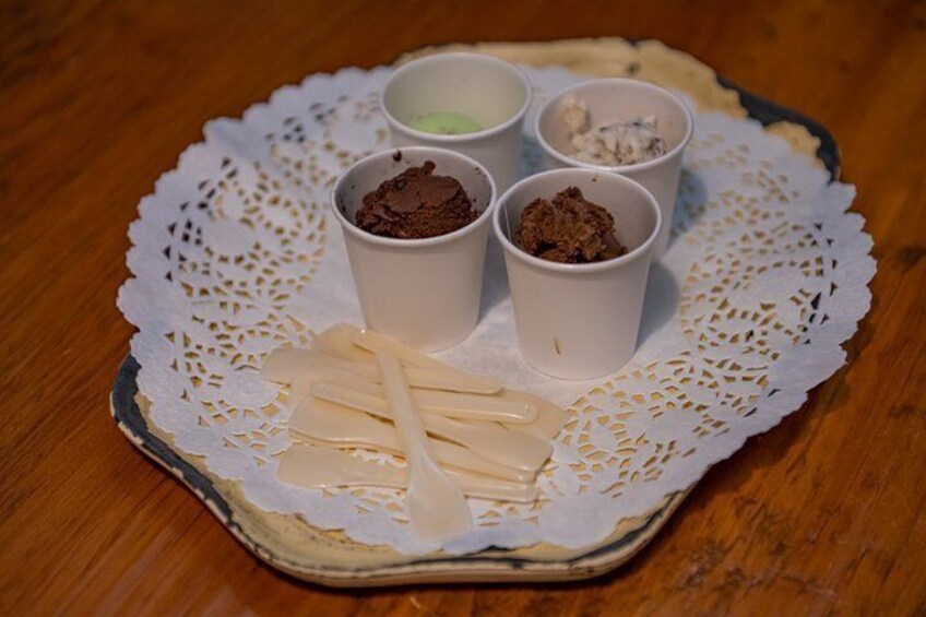 A plate with four small cups of different food items and some sticks on a lace doily. 2