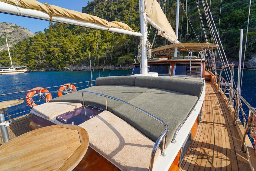 A sailboat with a cushioned deck, life rings, and a view of a forested coastline. 3