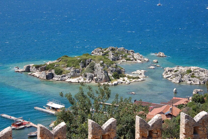 A coastal landscape with rocky islands, clear blue sea, and a dock with boats. 2