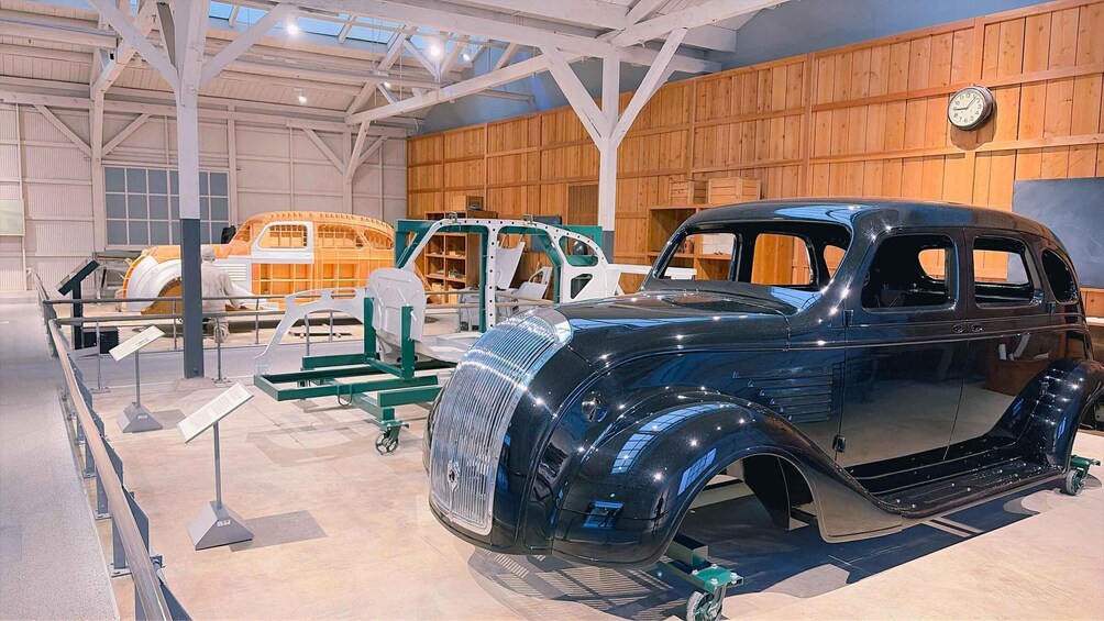 A vintage car on display in a museum with wooden walls and a clock. 1