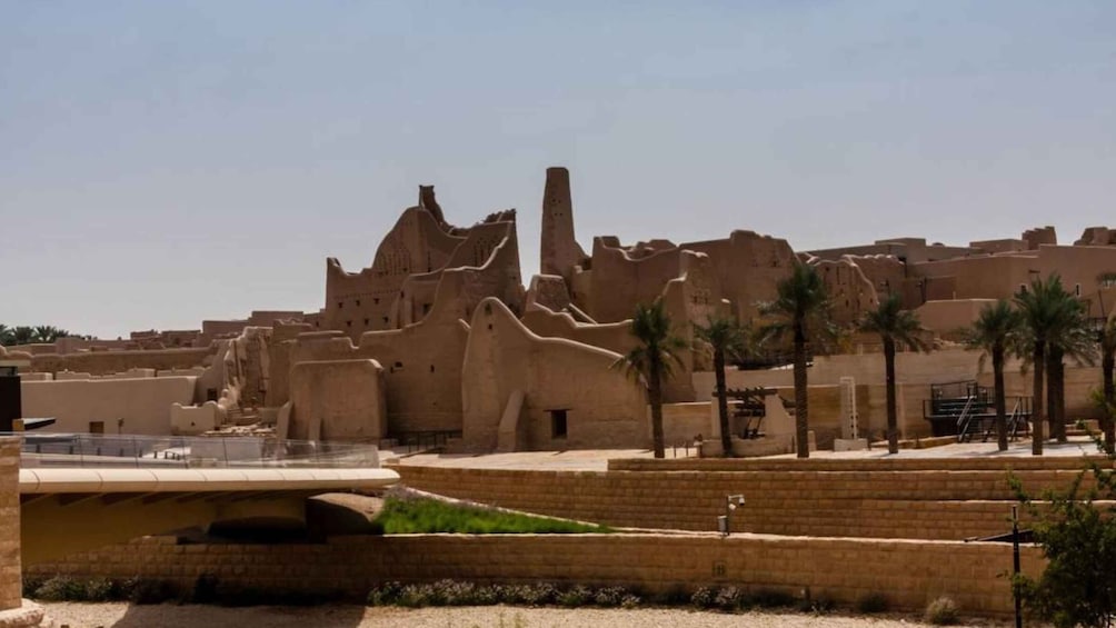 A desert landscape with ancient mud-brick structures and palm trees. 4