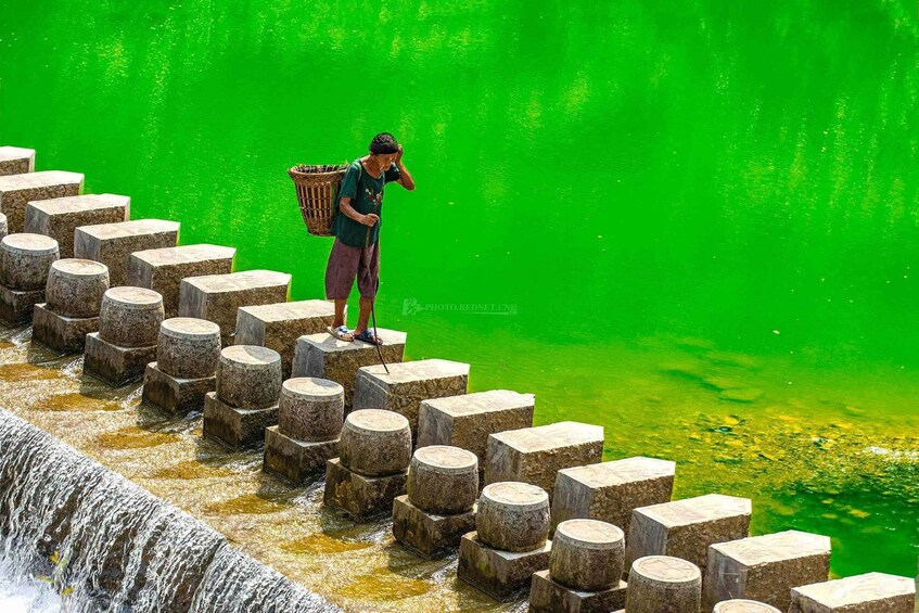 A person standing on a series of stone steps by a green body of water. 1