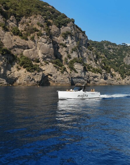 A white boat named 'mojito' on calm water with a rocky cliff in the background. 4