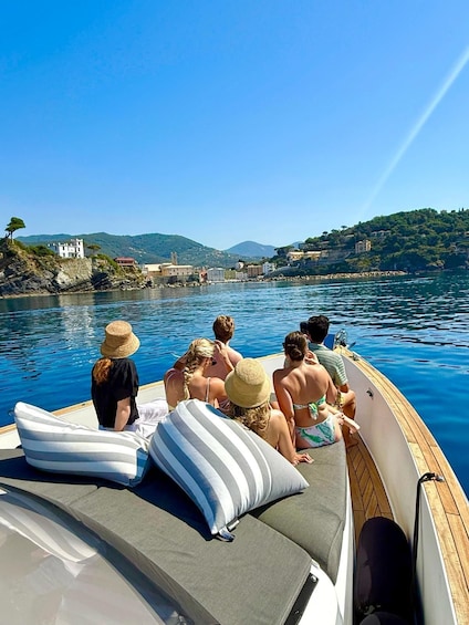 A group of people on a boat, a clear blue sky, and a coastline with buildings and hills in the background. 2