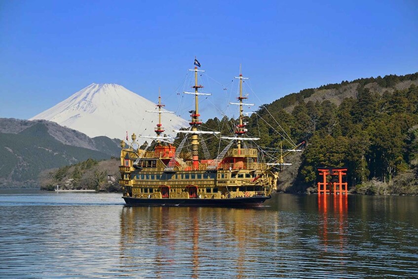 A large, ornate ship with multiple masts and a colorful design, docked near a forested shore with a mountain in the background. 2