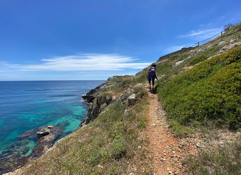 A hiker on a rocky coastal trail with clear turquoise waters. 4