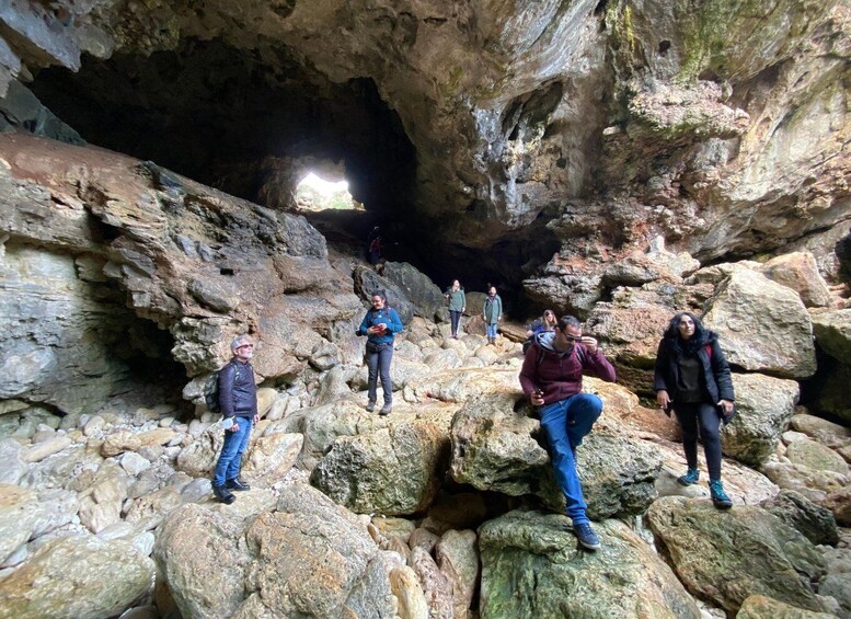 A group of people hiking in a rocky cave with large boulders and a narrow passageway. 3