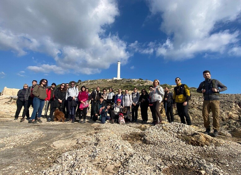 A group of people standing on rocky terrain with a lighthouse in the background. 1