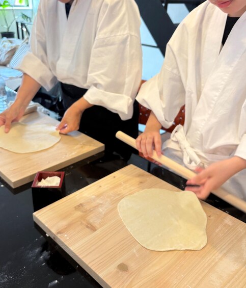 Two individuals in white lab coats rolling out dough on wooden boards. 5
