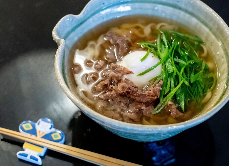 A bowl of ramen with noodles, a poached egg, beef, and green garnish. 5