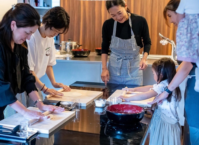 A group of people in a kitchen preparing food, with a rolling pin, bowls, and a black pan on the counter. 1